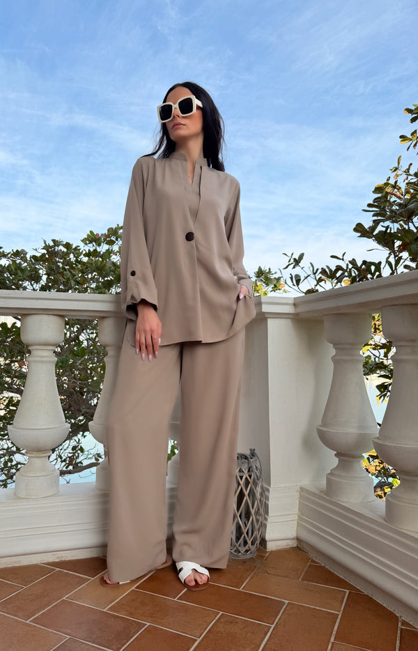 A woman wearing a beige co-ord set with a mandarin collar and wide-leg pants with pockets, standing on a balcony.